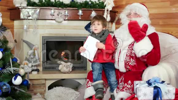 小男孩坐在圣诞老人腿上小男孩带着圣诞信访问圣尼古拉斯冬季住宅视频的预览图
