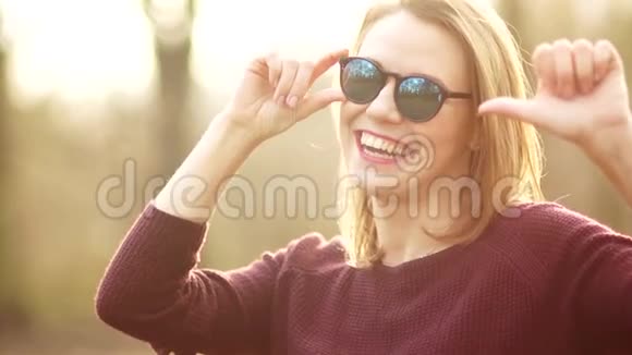 一个美丽的金发女郎带着白牙的微笑戴着太阳镜用拇指做了个手势好的视频的预览图
