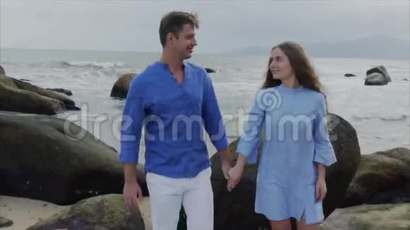 亲密的年轻幸福的情侣穿着蓝色的衣服正牵着手沿着海滨散步微笑着视频的预览图