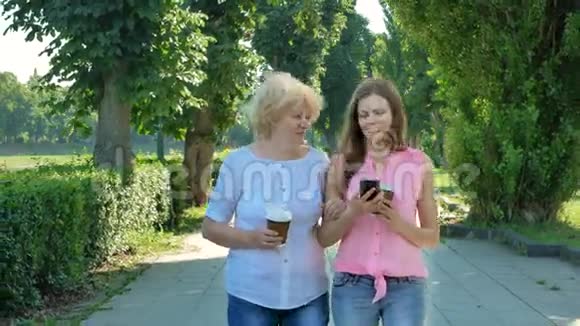 快乐的老年妇女和年轻妇女步行公园车道使用智能手机和喝咖啡成年母亲和女儿视频的预览图