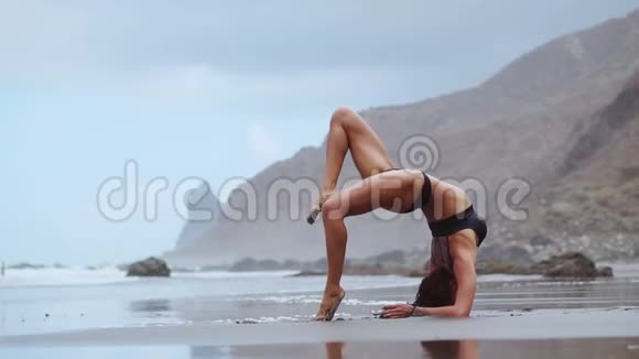 在海边做瑜伽的女孩站在他手上的一座姿势桥上视频的预览图