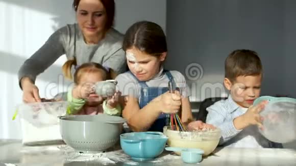 厨房里的杂声三个快乐的孩子把面团揉成馅饼妈妈帮他们筛面粉家庭烹饪视频的预览图