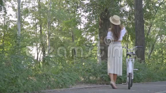 一个穿着白色裙子的黑发美女一件在公园里的衬衫手里拿着一辆城市自行车笑着回头看开心地笑着视频的预览图
