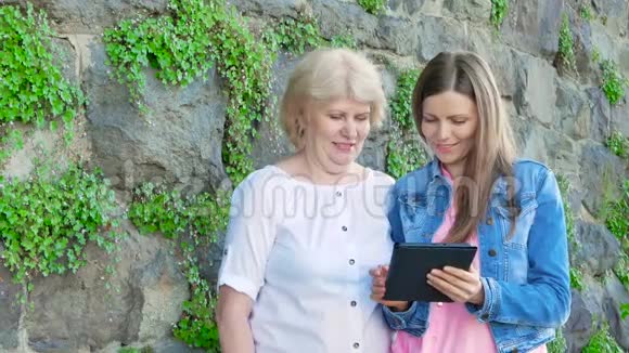 年长的女人和漂亮的年轻女孩使用平板电脑背景中野生石头的复古墙视频的预览图