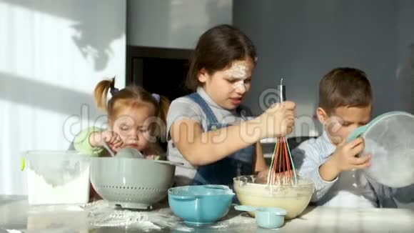 厨房里有三个孩子女孩搅动面团看着面团从花冠流出妈妈帮他们筛视频的预览图