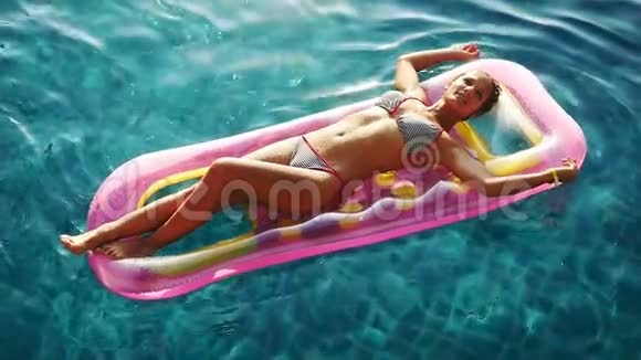 日落时分年轻漂亮的女人在游泳池里晶莹剔透的水中躺在充气床垫上享受视频的预览图