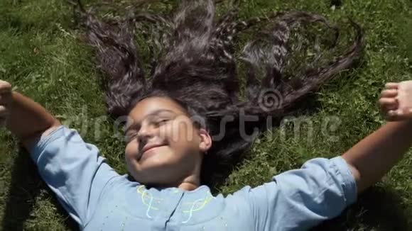 漂亮的长发女孩躺在公园的草地上慢动作高清高清视频的预览图