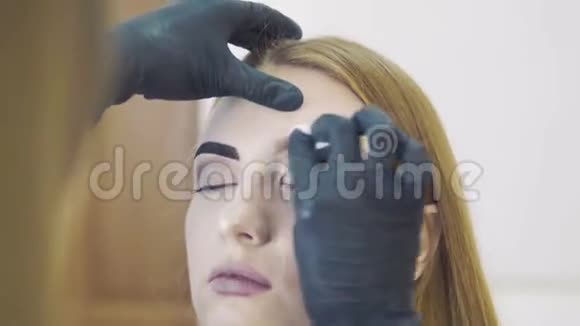发型师在美容院为卷发美女修眉用天然染料染眉视频的预览图