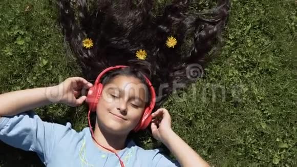 女孩躺在公园的草地上听着耳机里的音乐慢动作高清高清视频的预览图