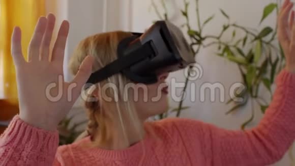 穿着粉红色毛衣的女人在家享受在现代扶手椅中使用虚拟现实护目镜视频的预览图