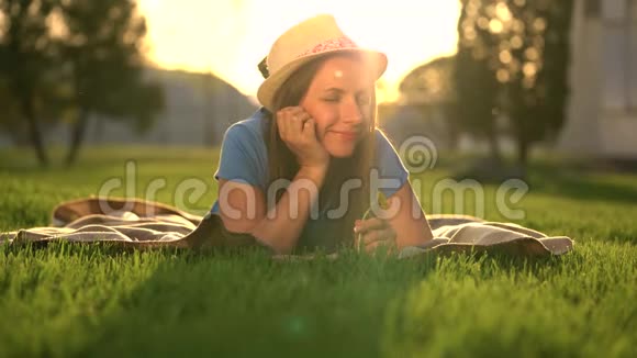 日落时分手里拿着蒲公英的女孩躺在公园的毯子上放松视频的预览图