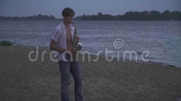 英俊的年轻人正在河岸上吹萨克斯管视频的预览图