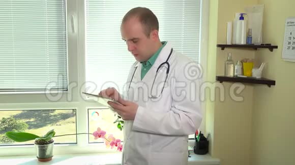 医院柜用数码平板电脑对着窗户听诊器的医生视频的预览图