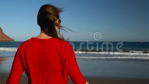 幸福的年轻女子穿着红色的连衣裙在日落时步行到海边的水上无忧无虑的现代生活理念视频的预览图