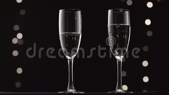 冷香槟倒在瓶子的两个透明玻璃里博克闪烁的黑色背景视频的预览图