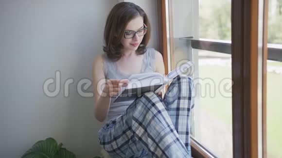 年轻女子坐在窗前在家看书视频的预览图