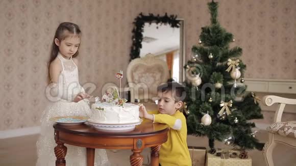可爱的小女孩和男孩把甜蜜的雪花放在圣诞蛋糕上漂亮的孩子在宽敞明亮的房间里靠近视频的预览图