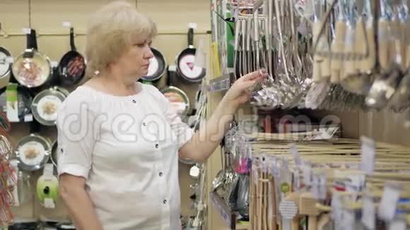 老妇人在超市里选择汤勺厨房配件在商店里购物高级女性视频的预览图
