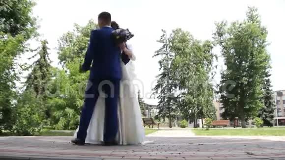 快乐的微笑时尚的新娘和新郎在夏天的绿色公园里散步带着鲜花跳舞玩得开心视频的预览图