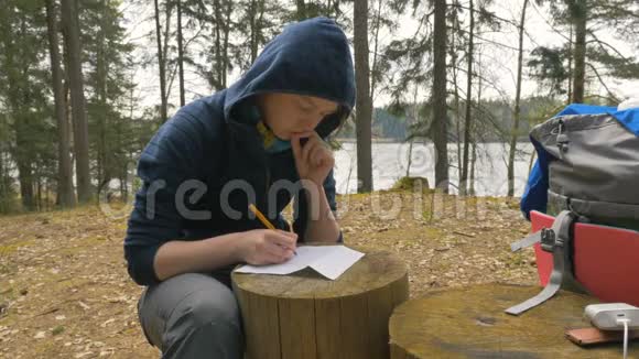 女孩正在森林里的树桩上写笔记视频的预览图