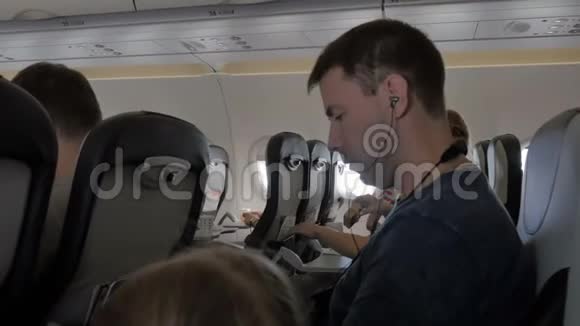 年轻人通过手机在耳机上听音乐一个商人正在飞机上看一段视频视频的预览图