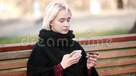 悲伤的金发女孩在外面表演交易黄金支付借记卡到智能手机视频的预览图