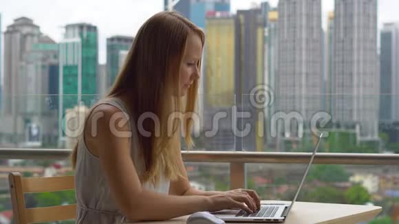 年轻女性自由职业者在阳台上的笔记本电脑上工作背景是一个充满摩天大楼的市中心视频的预览图