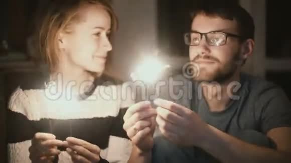一对年轻漂亮的夫妇晚上在家里坐着闪闪发光的男人和女人在一起接吻视频的预览图