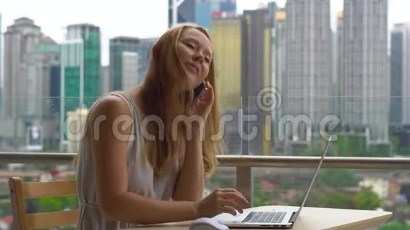 年轻女性自由职业者在阳台上的笔记本电脑上工作背景是一个充满摩天大楼的市中心她是视频的预览图