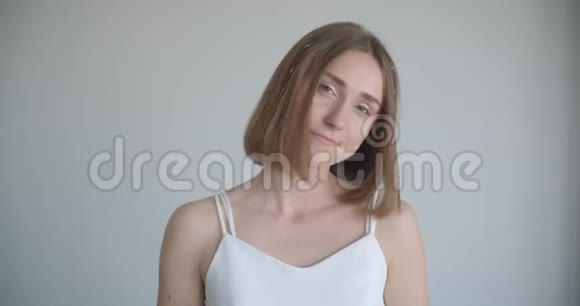 一位年轻漂亮的白种人女性戴着发环在室内的白色房间里看着摄像机视频的预览图