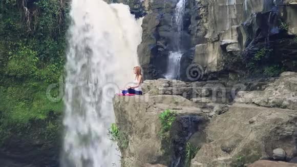 女子坐在瑜伽莲花的姿势旁边的泰根甘瀑布视频的预览图