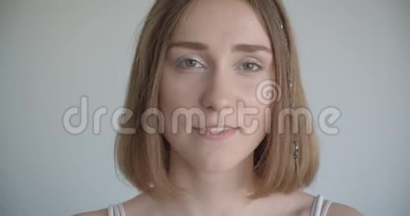 一位年轻漂亮的白种人女性的特写镜头她戴着发环和闪闪发光的妆容看着白色房间里的照相机视频的预览图