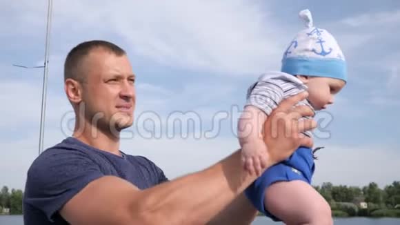 父亲的小男孩蓝天背景下坚强的双手美丽的男孩在湖上抱着儿子视频的预览图