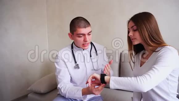 男医生向病人解释如何使用智能手表来监测健康并坐在医院办公室的沙发上视频的预览图