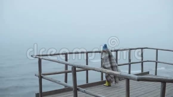小女孩穿着橡胶靴和格子呢站在靠近大海的木墩上在多雾的风天里独自一个孩子视频的预览图
