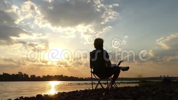 一个聪明的人坐在河堤上看着太阳落山视频的预览图