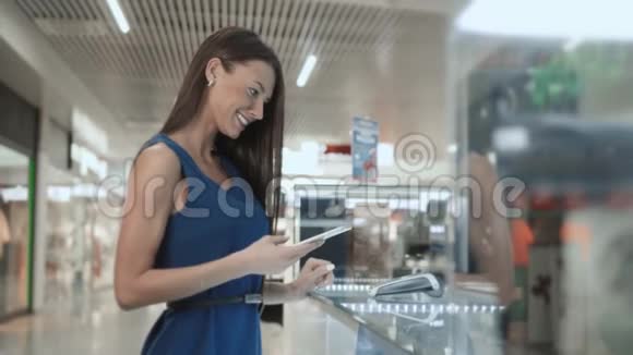 女士深色头发时尚模特购物手机NFC技术付费在超市商场机场候机楼视频的预览图