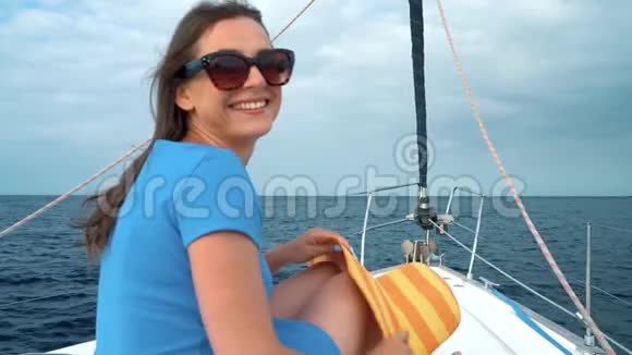 穿着黄色帽子和蓝色礼服的女人在海洋的夏季靠近灯塔的游艇上休息慢动作视频的预览图