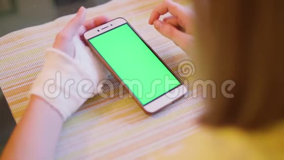 年轻的白种人金发碧眼左手断了看着绿色的智能手机屏幕近距离观看视频的预览图