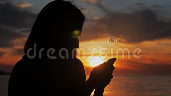 年轻女游客在海洋海滩日落时使用电话剪影一直连接互联网的概念视频的预览图