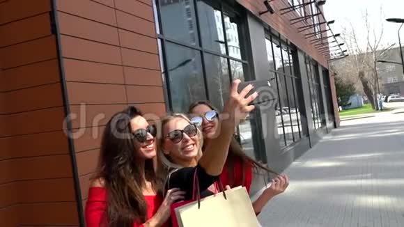 三个迷人的年轻女孩拿着购物袋路过商店附近女孩们笑着对着镜头笑视频的预览图