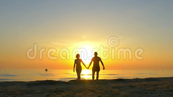 快乐的一对夫妇在夕阳的背景下手牵着手沿着海滩奔跑视频的预览图