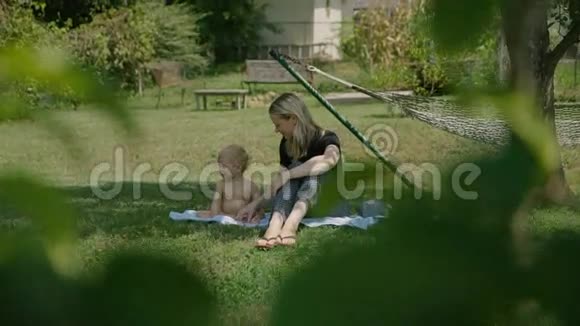 一位微笑的年轻女子躺在公园的草地上和她一岁的男孩玩耍视频的预览图