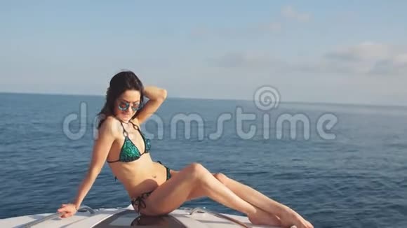 在阳光明媚的夏日穿着比基尼和太阳镜在游艇上摆姿势的年轻女孩视频的预览图