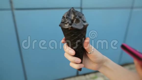 黑色木炭冰淇淋在一只蓝色背景的雌性手中视频的预览图