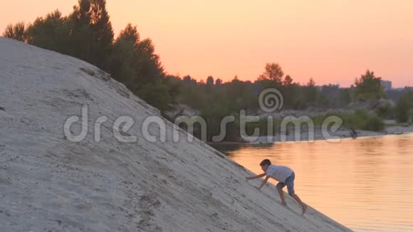 那个男孩在日落时爬上一座沙山孩子的积极休息视频的预览图