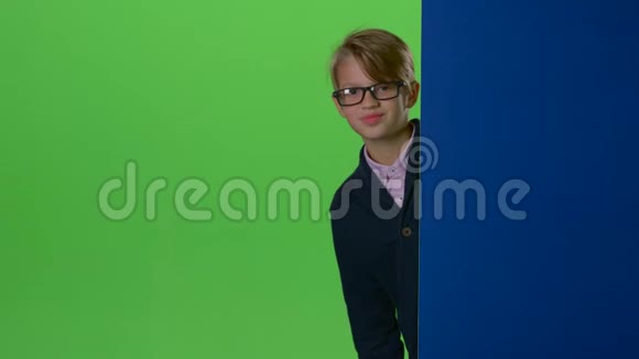 戴眼镜的快乐小男孩从绿色屏幕上的墙上窥视视频的预览图