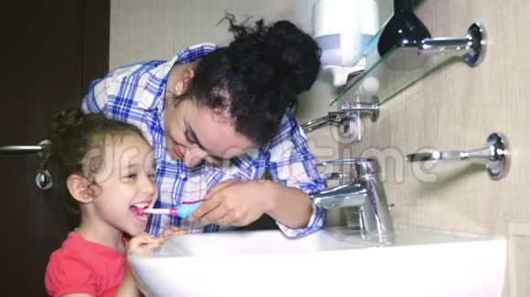 妈妈轻轻地刷牙她心爱的女儿的牙齿一个小女孩和她的母亲轻轻地清洁牙齿后吃4k视频的预览图
