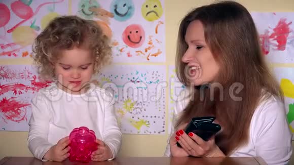 年轻的母亲和可爱的女儿把硬币放进储蓄罐视频的预览图