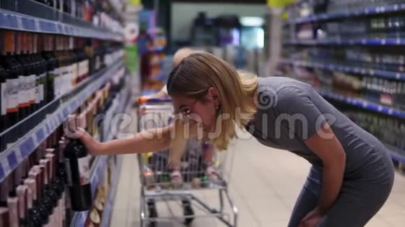 戴眼镜的漂亮女人正在超市的饮料部挑选一瓶酒而她的小宝贝视频的预览图